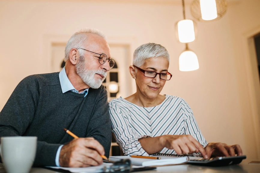 un jeune couple séniors assis à la table du salon utilise une calculatrice et un bloc notes